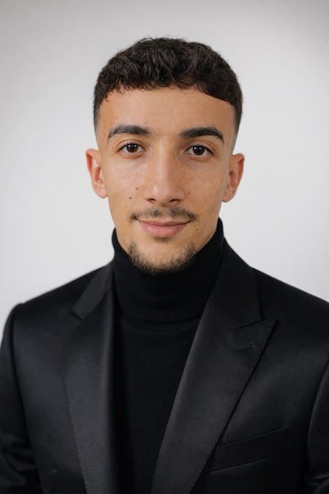 Retrato profesional de un hombre joven con cabello oscuro y barba usando blazer negro